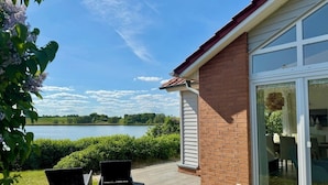 Une maison avec une façade en briques et de grandes portes vitrées, donnant sur un lac.