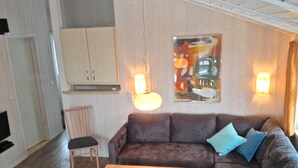 A cozy living room with a brown sofa, a wooden coffee table, and a chair. There is a cabinet and a painting on the wall. - Cozy lodge on a hillside with Schleiblick | Sauna | Fireplace | Free Wi-Fi (Kosel)