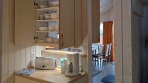 A kitchen with wooden cabinets, a toaster, a coffee maker, and a dining area with chairs and a table. - Cozy lodge on a hillside with Schleiblick | Sauna | Fireplace | Free Wi-Fi (Kosel)