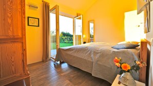 A bedroom with a bed, a nightstand with a vase of flowers, and a view of a garden through an open door. - Schlei Resort Marina sleeves (Kosel)