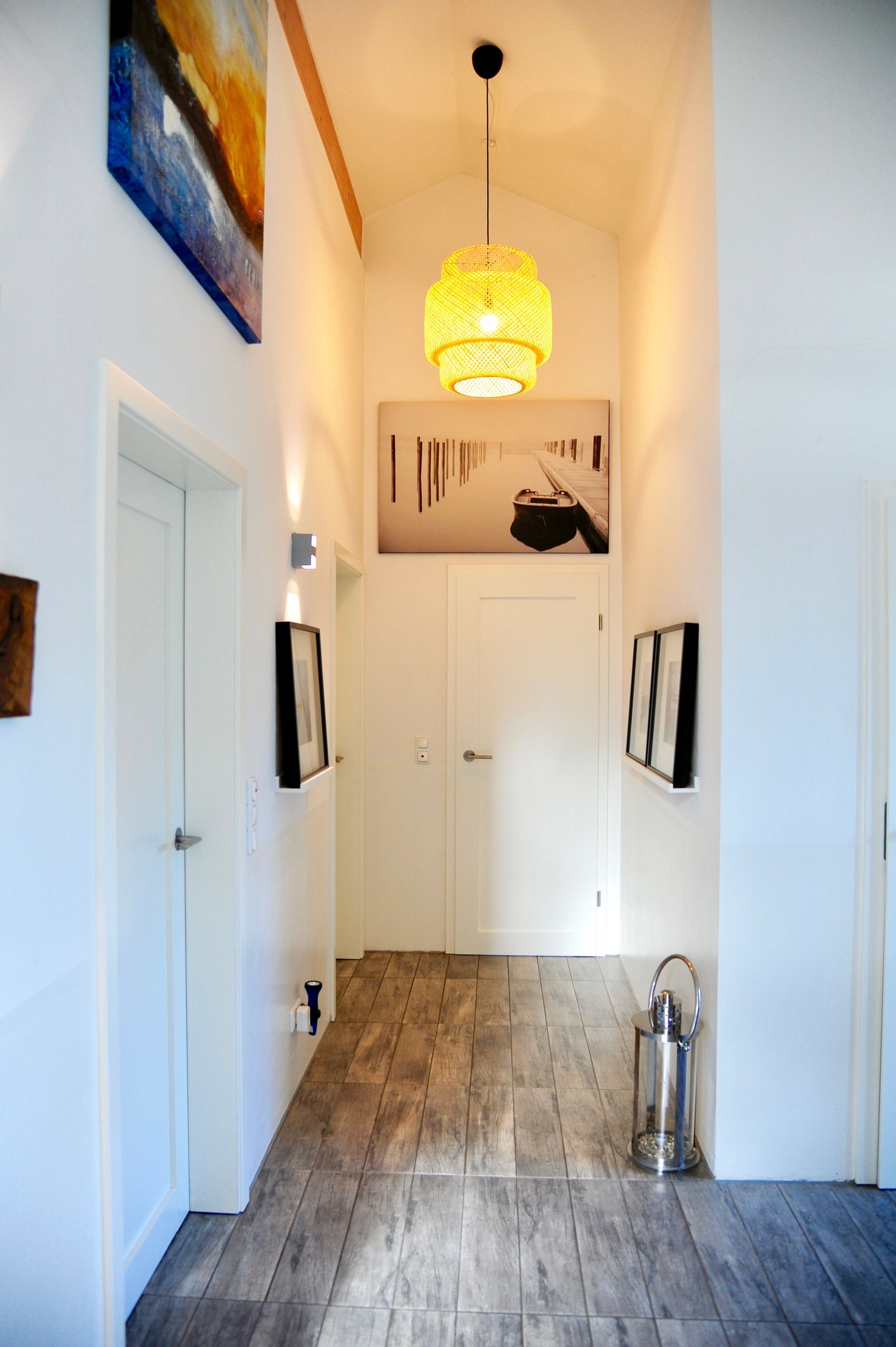 Un corridoio con pavimento in legno, porte bianche e un lampadario.