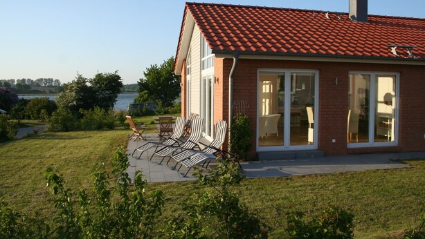 Ein Haus mit rotem Ziegeldach, einer Ziegelaußenwand und einer Terrasse mit Liegestühlen.