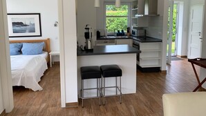 Eine moderne Küche mit Kochinsel, ein Essbereich mit Barhocker und ein Schlafzimmer mit Bett und einem gerahmten Bild.