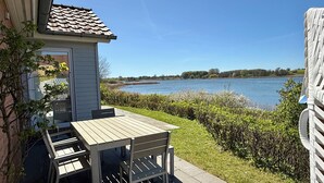 Un patio con una mesa, sillas, un cobertizo pequeño y vistas a un lago.