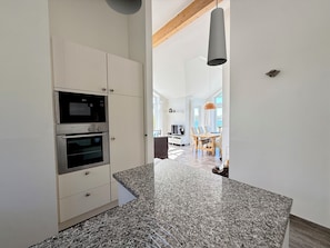 A modern kitchen with built-in appliances, a granite countertop, and a view into the dining area.