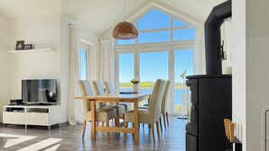 Una cocina moderna con una estufa negra, una mesa de comedor con sillas, un televisor sobre un mueble blanco y un ventanal con vistas al exterior.