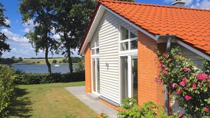 Ein Haus mit rotem Ziegeldach, weißer Fassade und einem Backsteinbereich. Es hat ein großes Fenster und eine Tür, mit einem Garten davor.