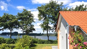 Ein Haus am Seeufer mit rotem Dach, umgeben von üppigem Grün und freiem Blick auf den See.