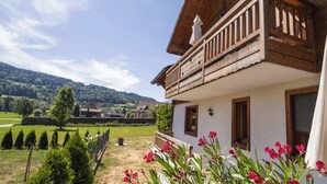 Un chalet doté d’un balcon en bois, d’un jardin fleuri et offrant une vue sur une vallée.