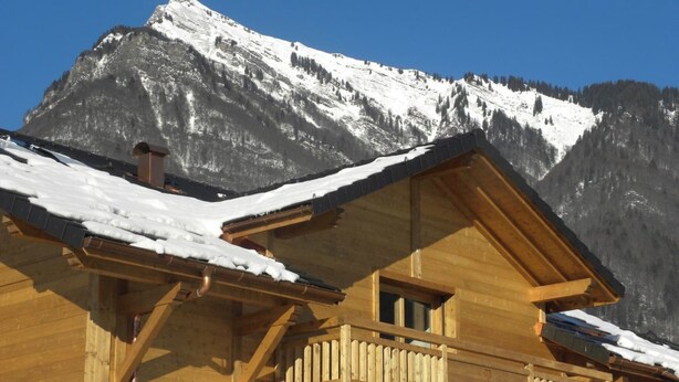 Un chalet en bois doté d’un balcon, d’un toit enneigé et surplombant un paysage montagneux.