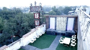 A rooftop terrace with a sign reading "HOTEL B" and a seating area with white chairs and tables. - Hotel Blessings (New Delhi)