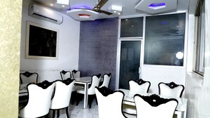 A dining area with white chairs, a marble floor, and a ceiling fan. - Hotel Blessings (New Delhi)