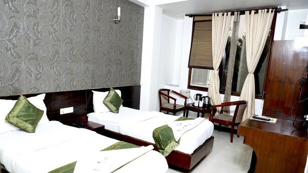 A hotel room with two beds, a desk, a chair, a wardrobe, and a window with curtains. - Hotel Blessings (New Delhi)
