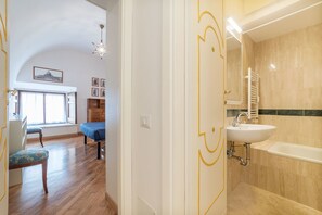 A room with a wooden floor, a bed, a window, a sink, and a bathtub. - Campitelli Fascinating Apartment (Rome)