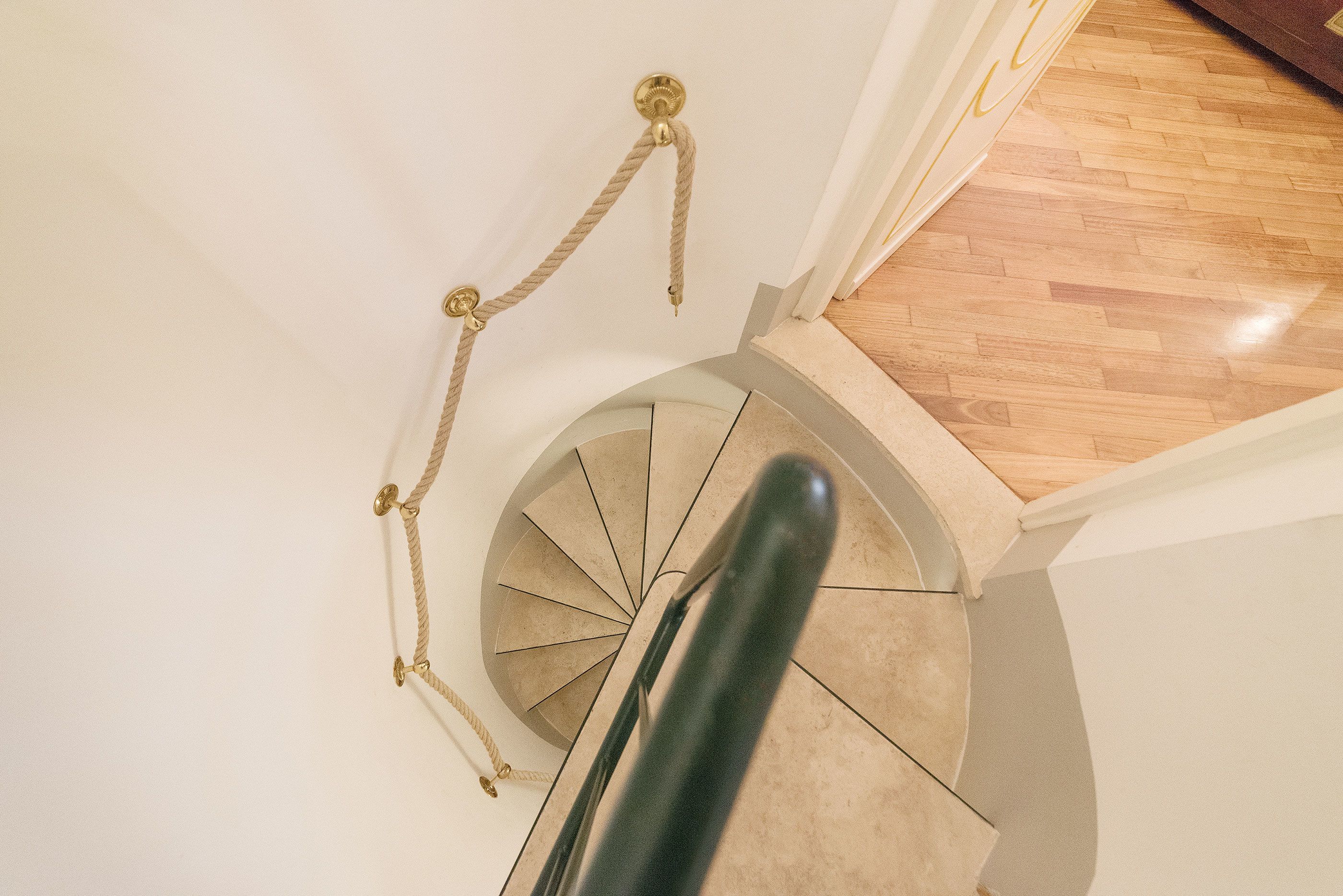 A spiral staircase with a rope handrail and a wooden floor landing.