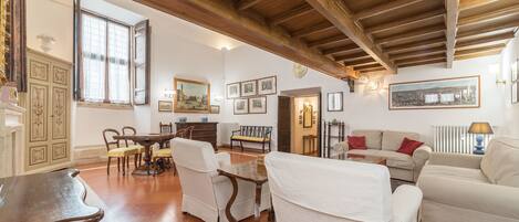 A spacious living room with a high wooden ceiling, a dining area with a wooden table and chairs, and a cozy seating area with a sofa and armchairs.
