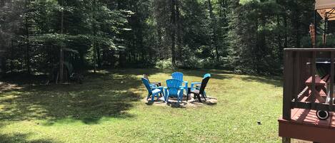 An outdoor seating area with blue chairs and a table, surrounded by a forested area.