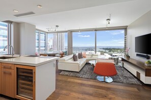 A modern living room with a large window, a flat-screen TV, and a kitchen area with a sink and oven.
