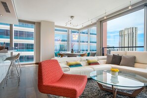 A modern living room with a glass coffee table, a red chair, a white sofa, and a dining area with a table and chairs. - Luxurious Two bedroom Unit with Panoramic Ocean View in ONE Ala Moana (Honolulu)