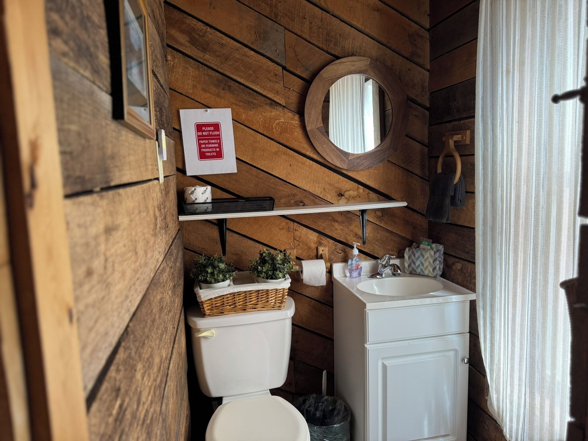 A wooden cabin bathroom with a toilet, sink, and a sign prohibiting flushing paper towels or feminine products.