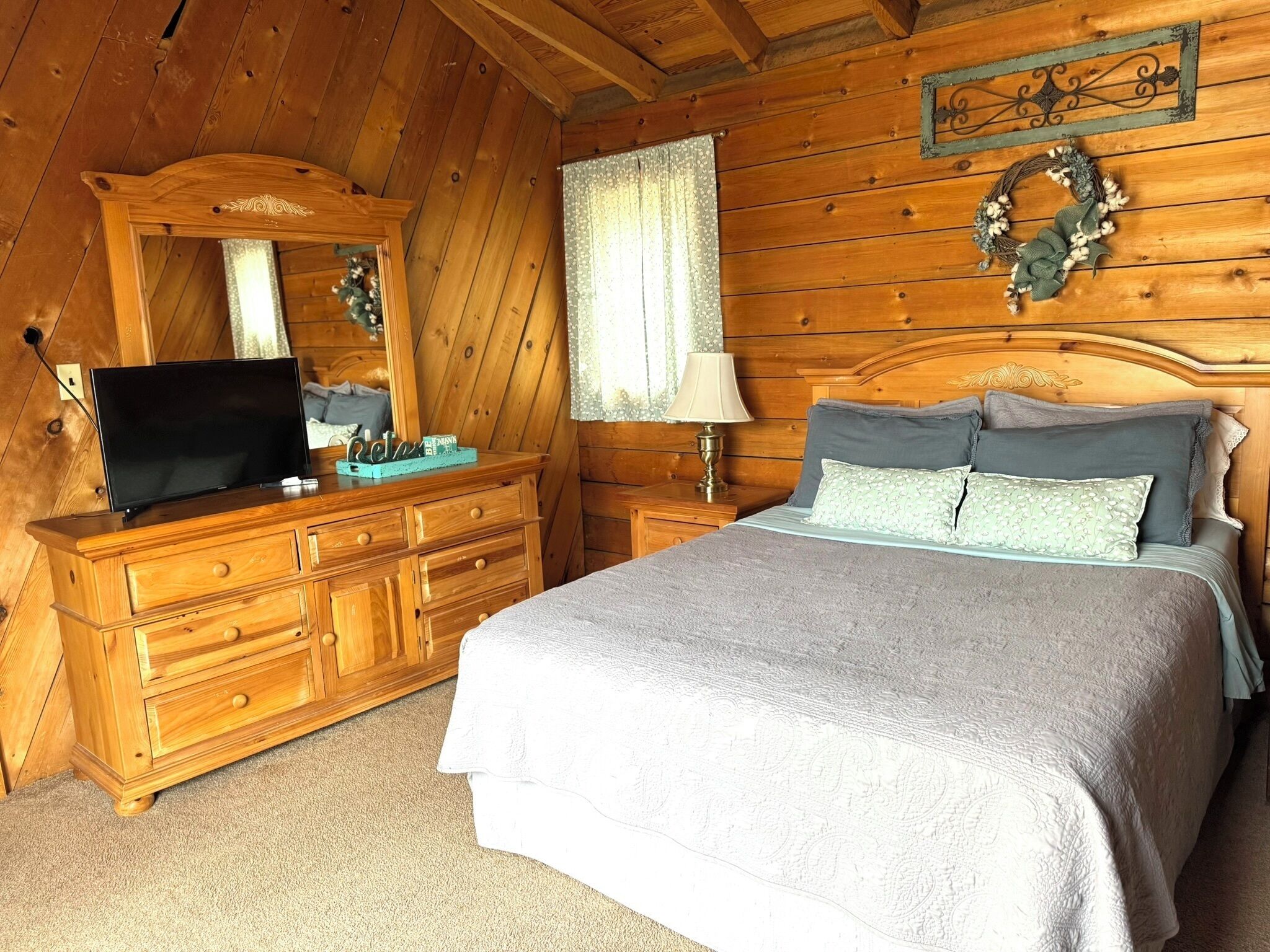 A wooden cabin bedroom with a bed, dresser, TV, and a mirror.