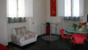 A living room with a white sofa, red chairs, a glass table with a vase of flowers, and a red abstract painting on the wall. - Luxury Rose (Florence)