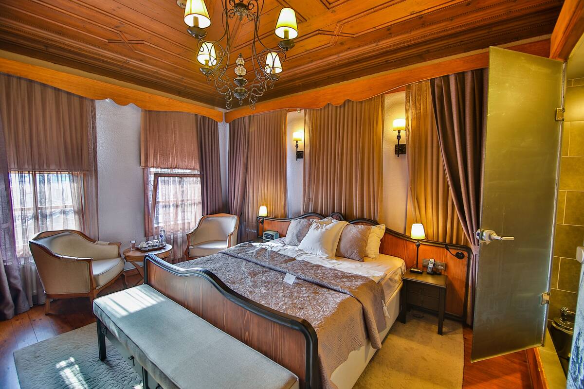 A hotel room with a large bed, bedside tables, a chair, a desk, and a chandelier.