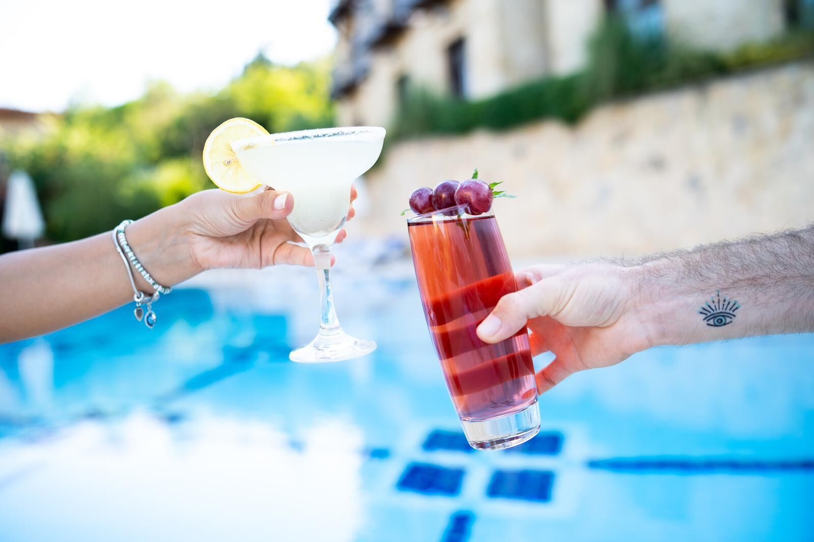 Two people holding drinks by a poolside.