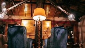 Ein gemütlicher Raum mit zwei bequemen, blauen Ohrensesseln, einer hohen Stehlampe und einer Holzbalkendecke.