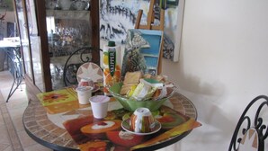 Une table à manger recouverte d’une nappe colorée, avec un saladier de fruits, ainsi que divers plats et tasses.