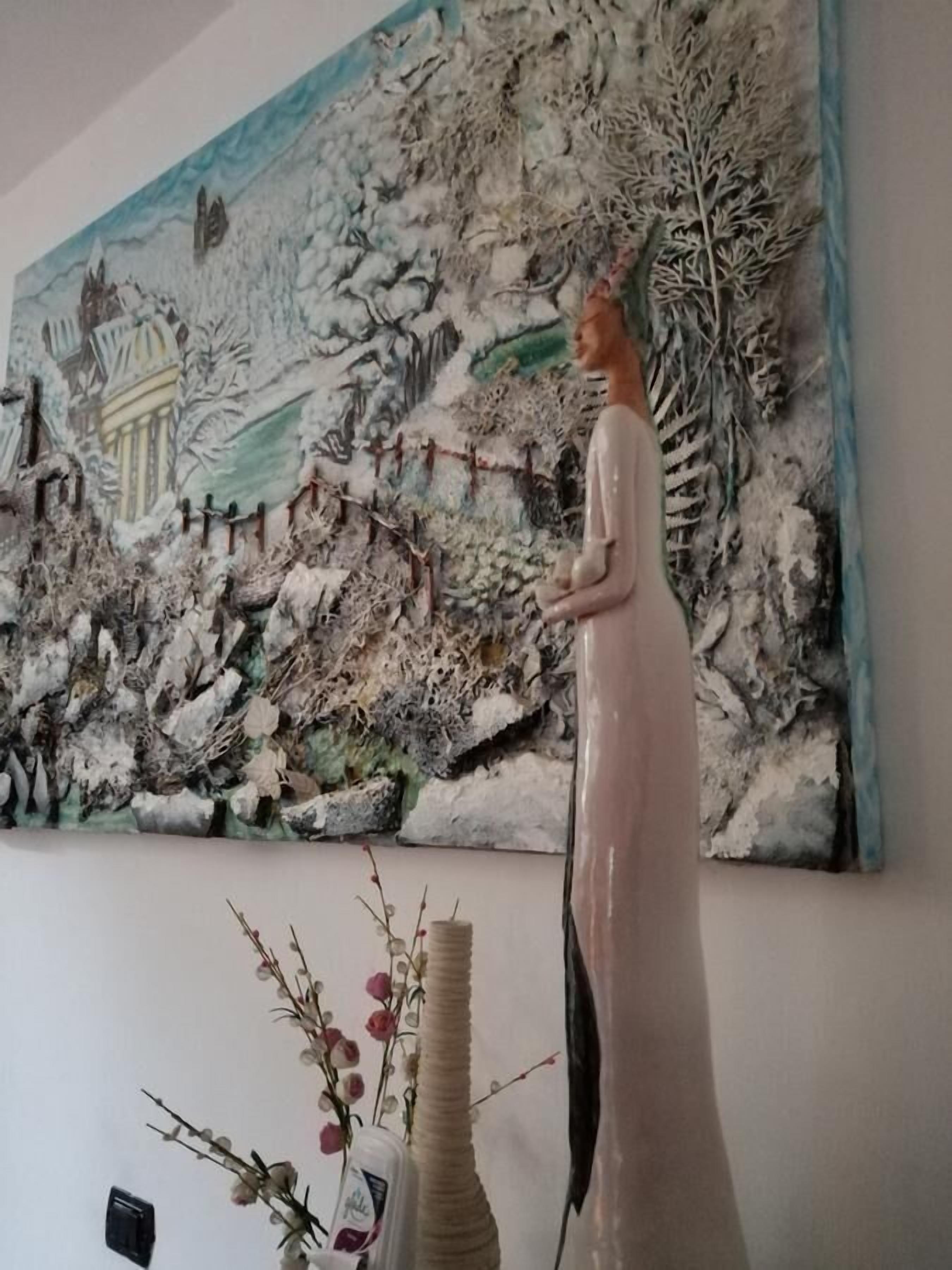 Una habitación con un cuadro abstracto grande en la pared, un jarrón alto con ramas y flores, y una estatua de una mujer.