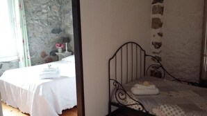 A bedroom with a bed, a nightstand, and a stone wall. - L'Envolée (Belvianes-et-Cavirac)
