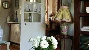 A room with a floral tablecloth, a vase of white flowers, a wooden bookshelf, and a mirror on the wall. - L'Envolée (Belvianes-et-Cavirac)