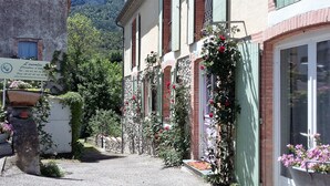 A narrow street with buildings on either side, featuring a sign for a hotel, a stone bollard, and a flower pot. - L'Envolée (Belvianes-et-Cavirac)