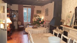 A cozy dining area with a round table, chairs, a vase of flowers, and a fireplace. - L'Envolée (Belvianes-et-Cavirac)