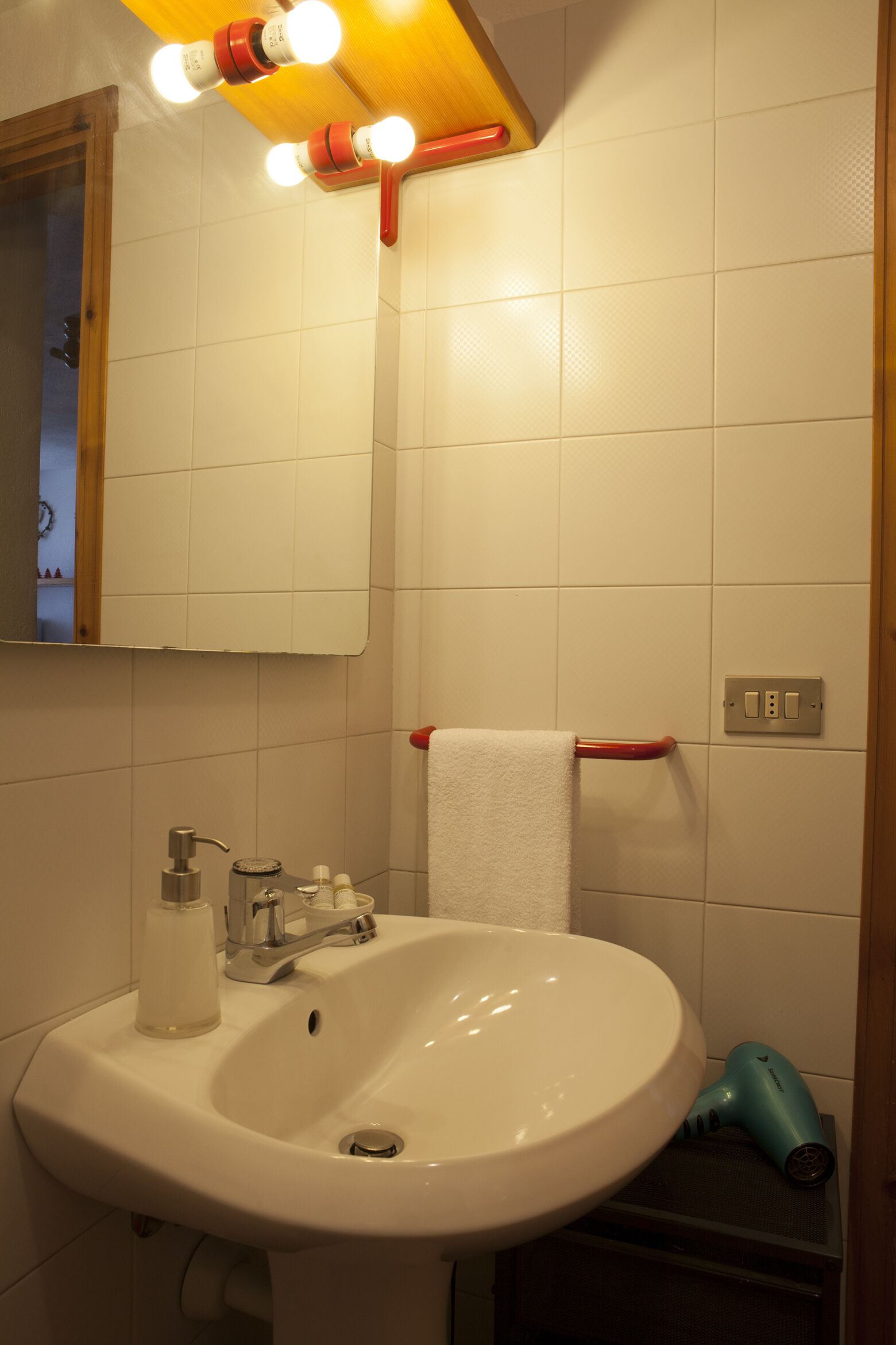 Un bagno con lavandino bianco, uno specchio e un porta asciugamani.