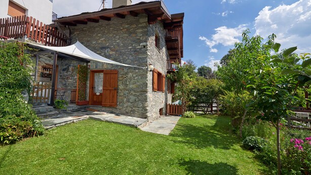 A stone house with a wooden balcony, a white awning, and a well-maintained garden. - Le Rosier B&B e Appartamento (Saint-Vincent)