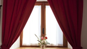 A window with red curtains, a wooden window sill, and a vase with flowers. - Le Rosier B&B e Appartamento (Saint-Vincent)