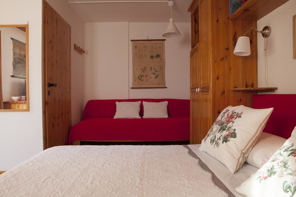 Une pièce avec un canapé rouge, un lit blanc orné d’oreillers à motifs floraux, des murs en bois et une estampe botanique suspendue au mur.