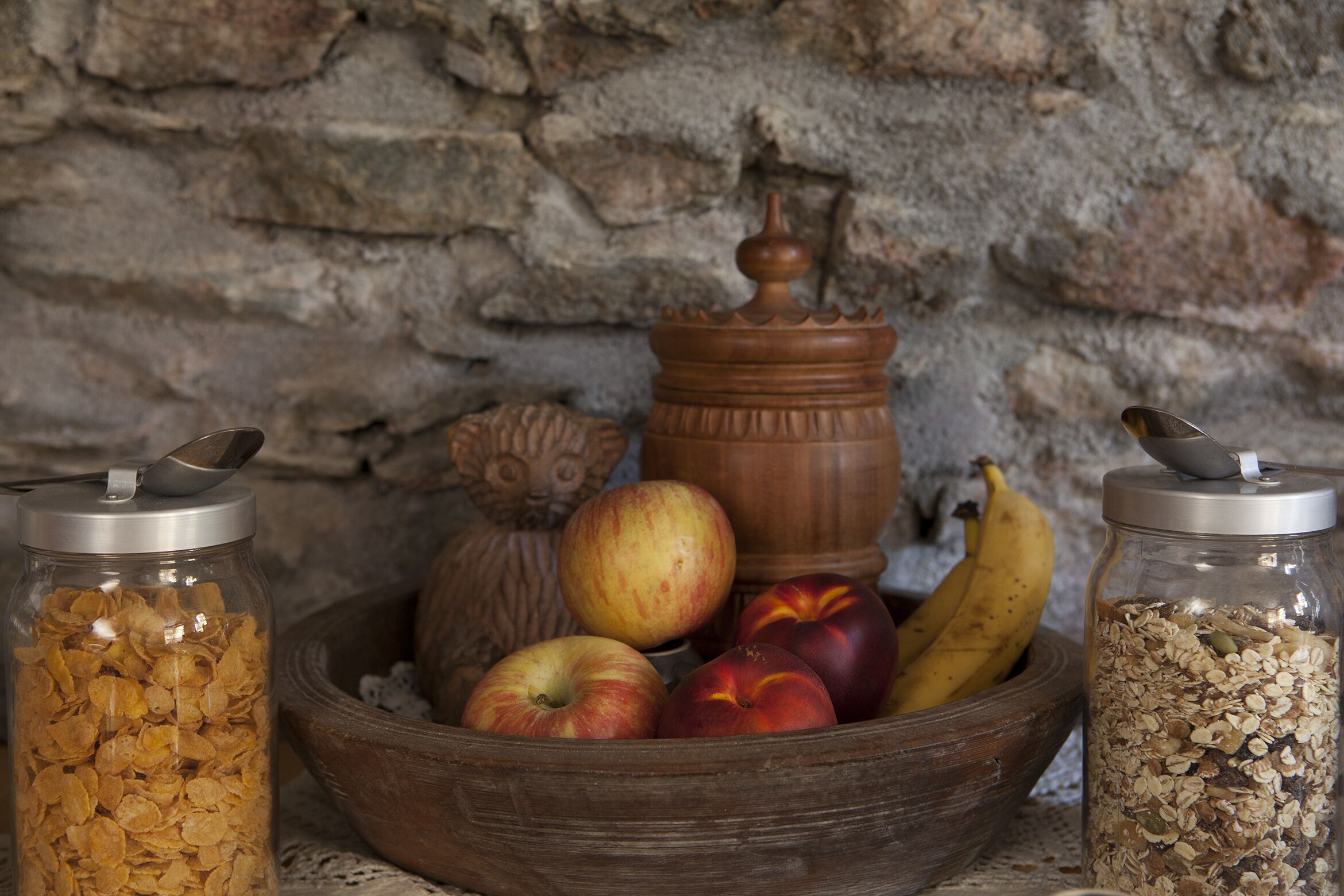A wooden bowl filled with apples and bananas, a jar of cereal flakes, and a jar of oats.