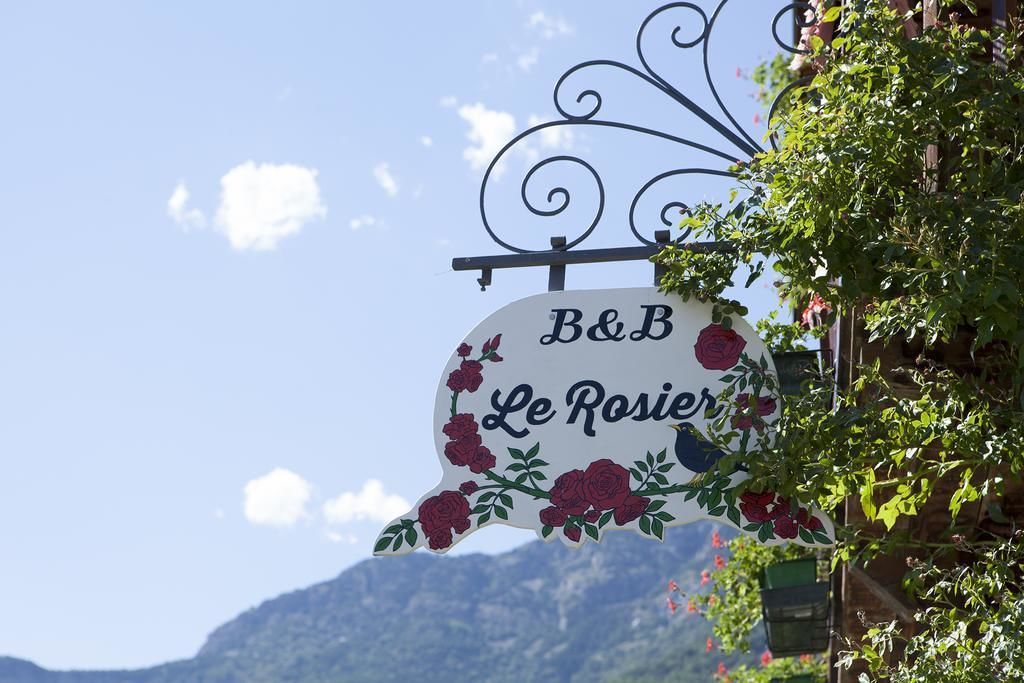 Een bordje voor B&B Le Rosier, met een berg op de achtergrond.