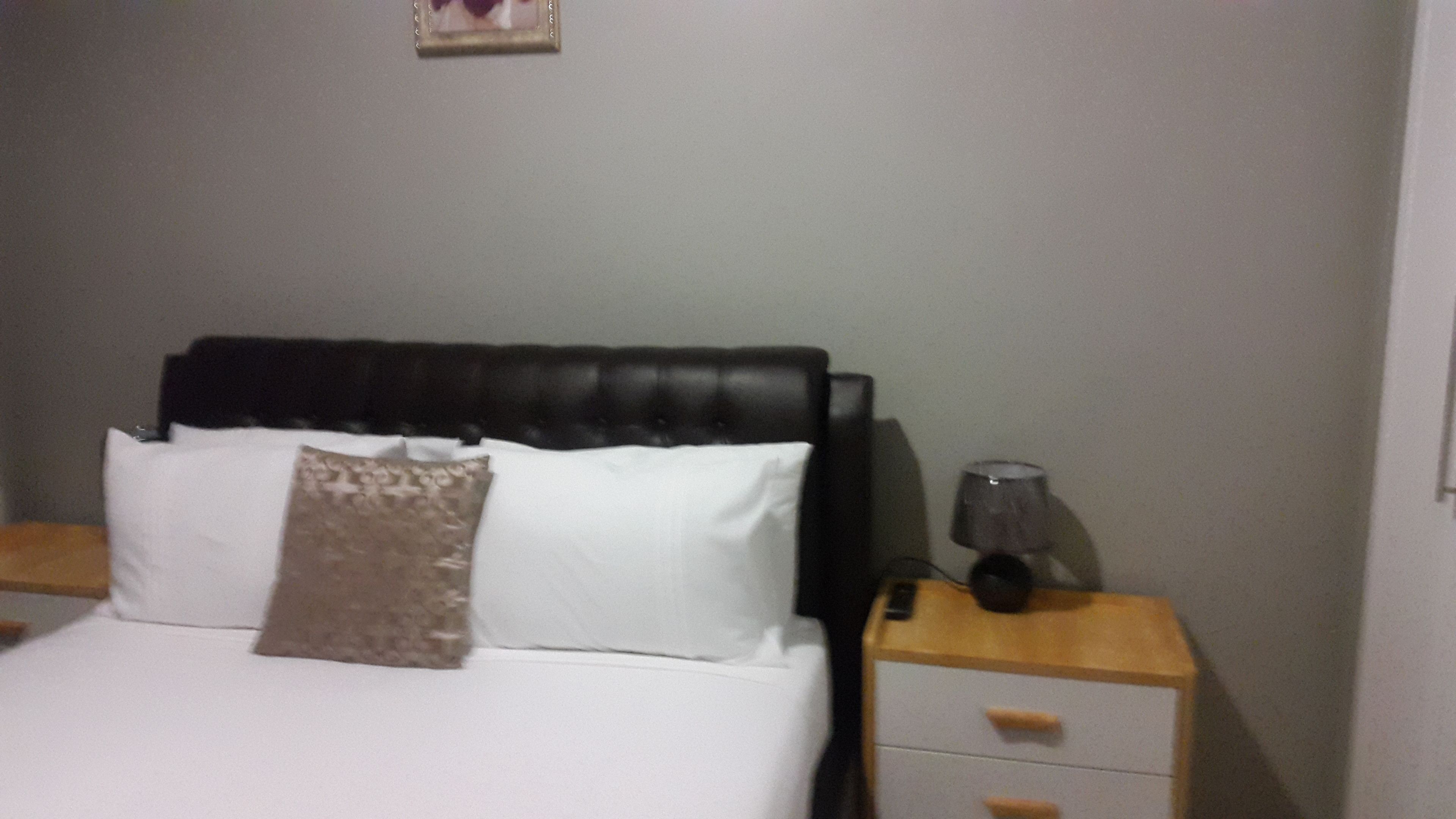 A bed with white linens and a brown pillow, a black headboard, and a bedside table with a lamp.