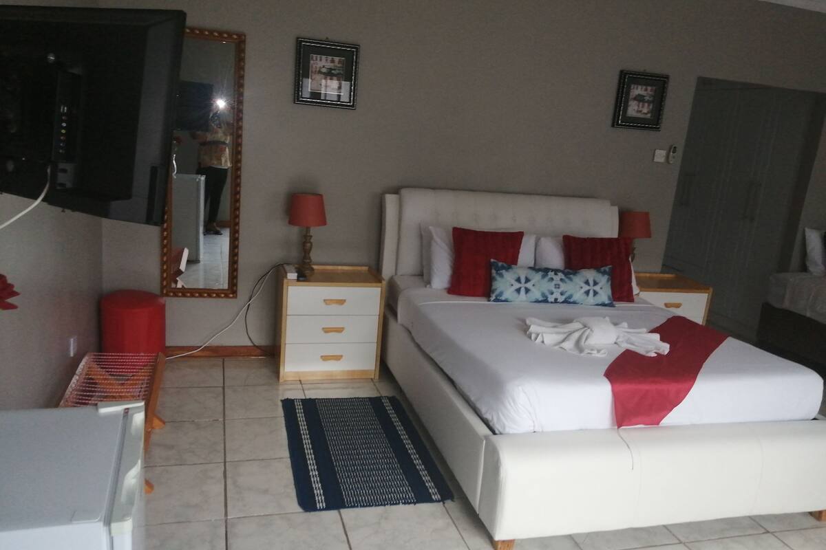 A bedroom with a bed, a nightstand, a mirror, and a wall-mounted TV.