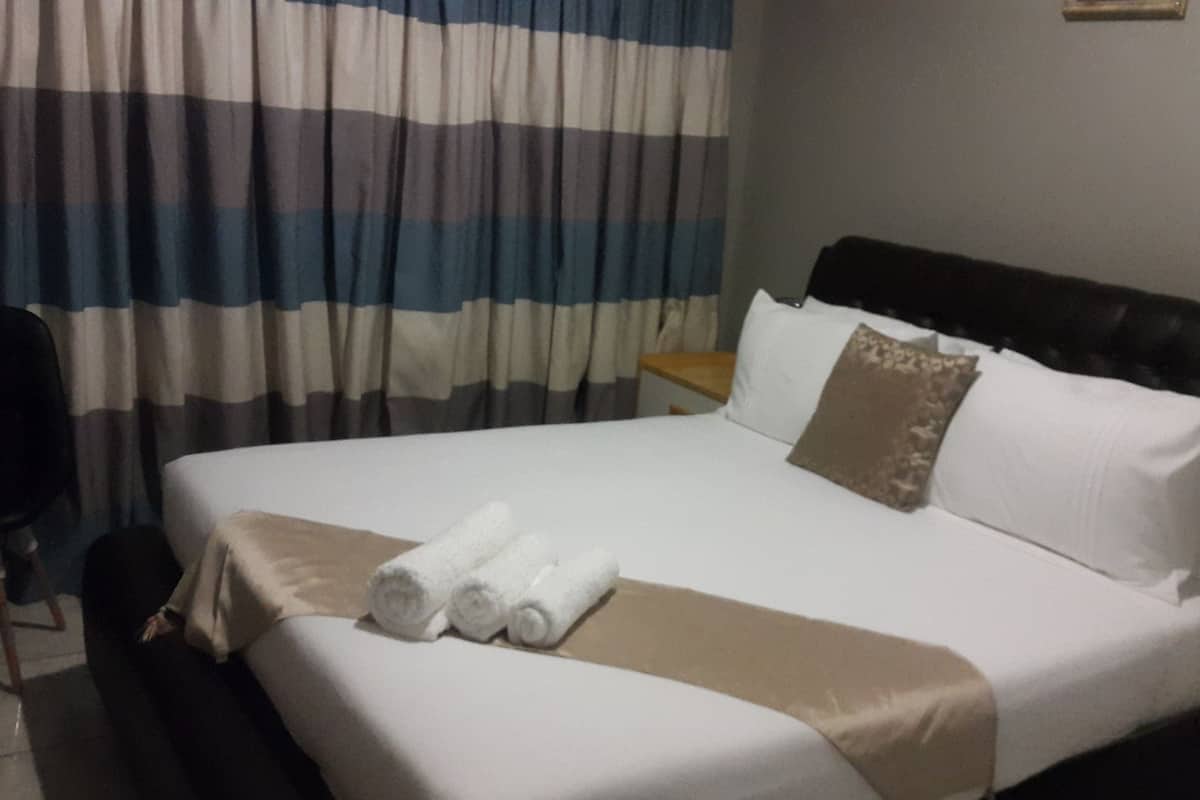 A hotel room with a bed, a chair, a nightstand, and a curtain.