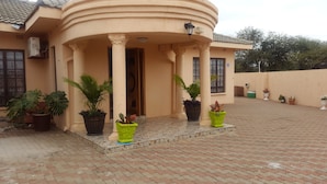 A building with a curved facade, a covered entrance with columns, and a paved courtyard with potted plants. - Tintech Bed & Breakfast (Francistown)