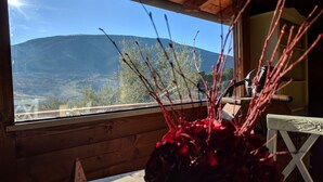 A wooden cabin interior with a view of mountains through a window, a wooden table, and a vase with red branches. - Agriturismo Sole Luna (Assisi)