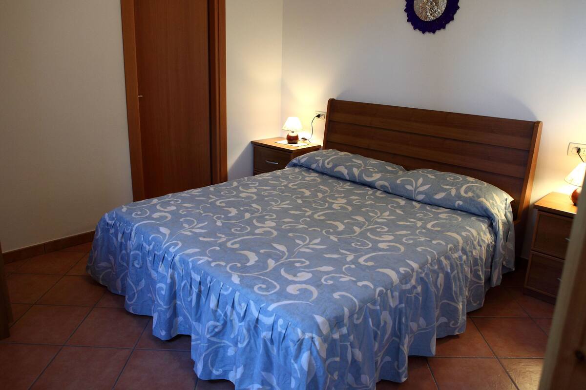 A bedroom with a bed, nightstands, and a wall decoration.