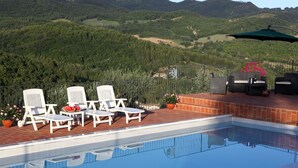 A swimming pool with white lounge chairs and a barbecue area, surrounded by a brick deck and overlooking a forested landscape. - Agriturismo Sole Luna (Assisi)