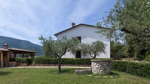 A white building with a stone base and a tiled roof, surrounded by a well-maintained lawn and trees. - Agriturismo Sole Luna (Assisi)