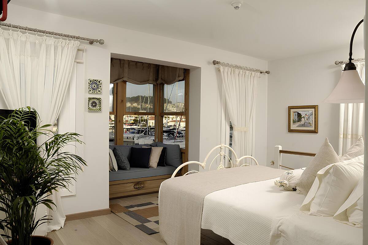 Une chambre à coucher avec un lit, un coin fenêtre donnant sur le port, une plante en pot et une lampe.